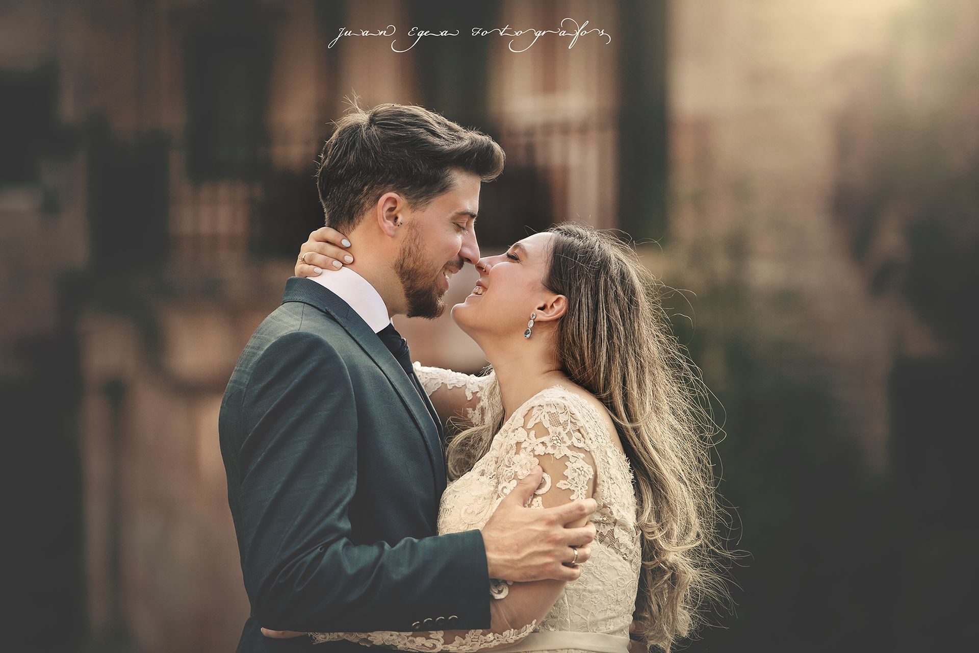 Pareja abrazándose, novia con vestido de encaje, novio con traje, besándose, fondo suave.