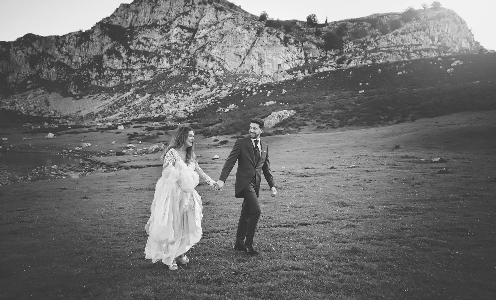Pareja de la mano caminando por el campo con la montaña al fondo. Blanco y negro.