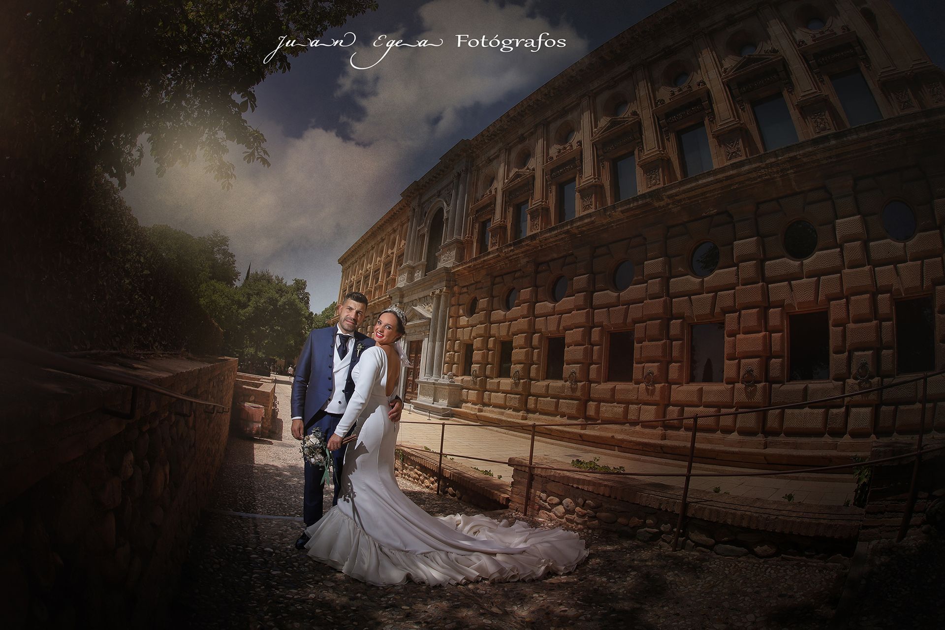 Los novios posan frente a un edificio ornamentado. La pareja sonríe y el cielo brilla.