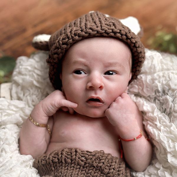 Bebé con traje de ciervo de punto marrón y brazos en alto.