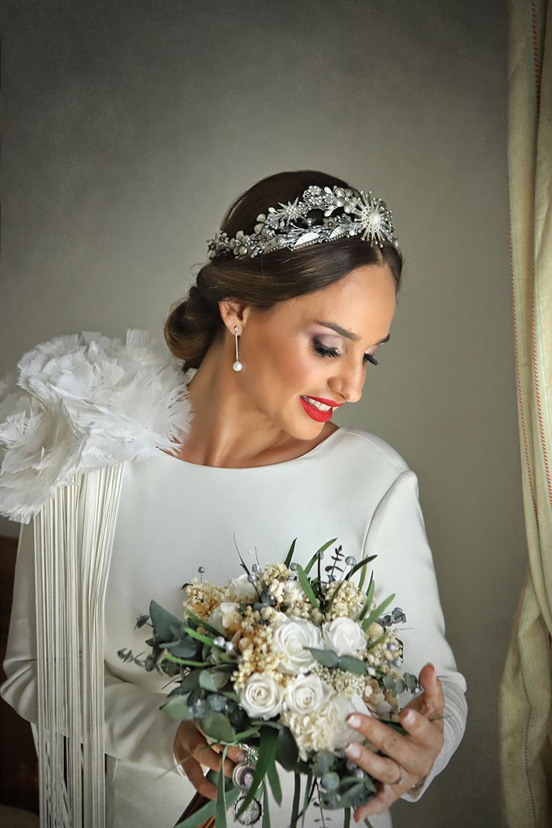 Novia con vestido blanco y tiara sosteniendo ramo, sonriendo.
