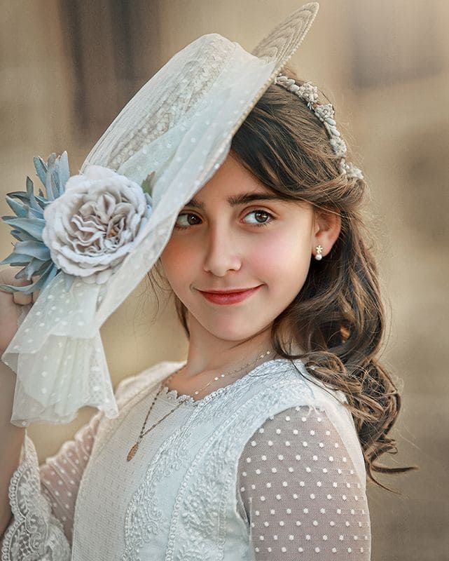 Niña con vestido blanco y sombrero, sonriendo, mirando hacia un lado.