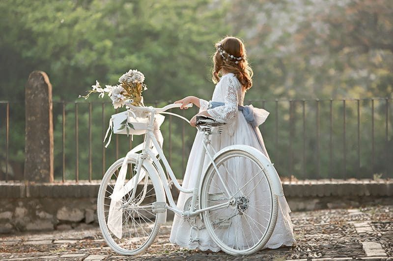 Novia con vestido blanco con bicicleta decorada, al aire libre.