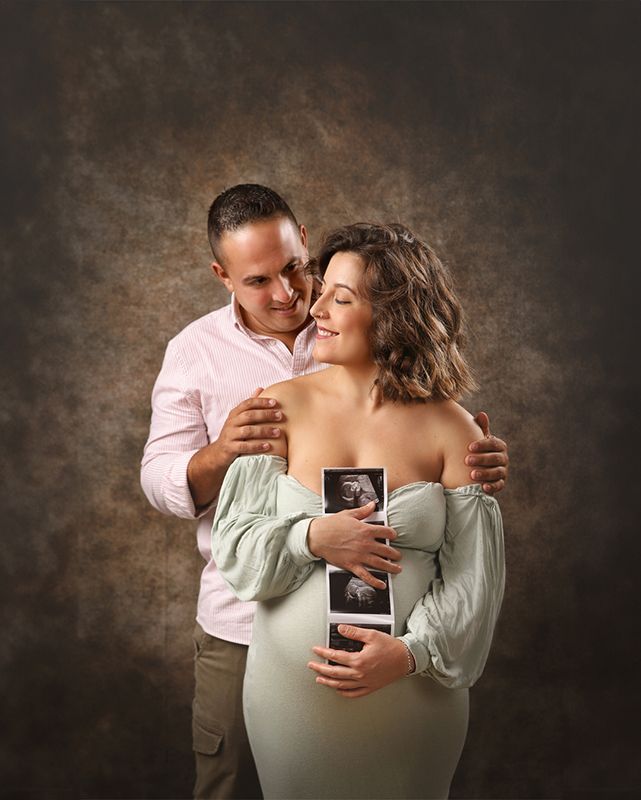 Mujer embarazada y su pareja sostienen imágenes de ultrasonido. Se abrazan, con un fondo marrón.