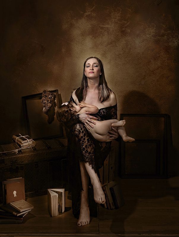 Mujer con bata de encaje amamantando a un bebé, con libros en un entorno en tonos sepia.
