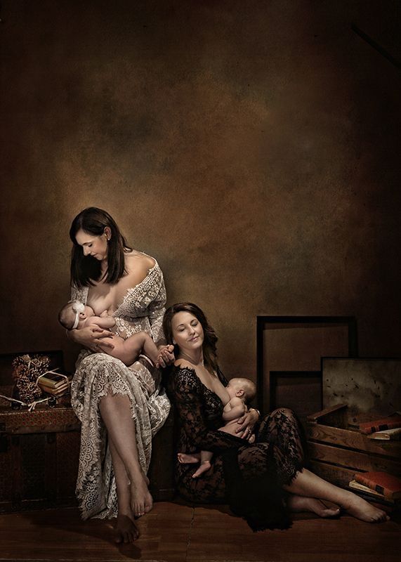 Dos mujeres con elegantes vestidos amamantando a sus bebés. Fondo marrón; iluminación cálida.