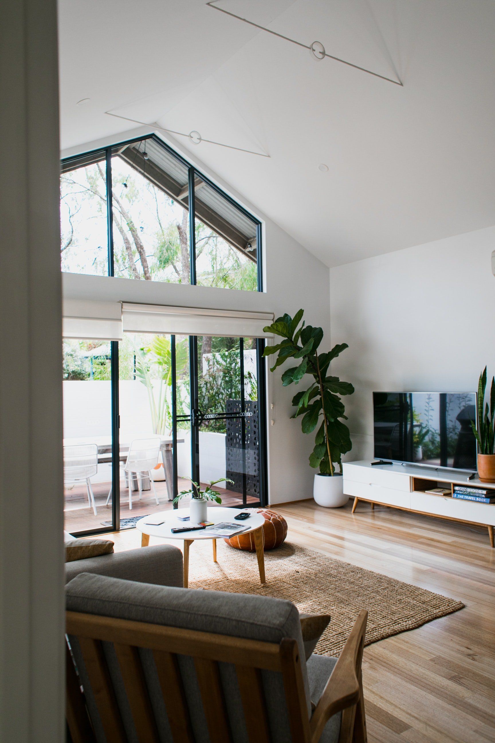 Sala de estar con grandes ventanales, planta, piso de madera y decoración neutra.