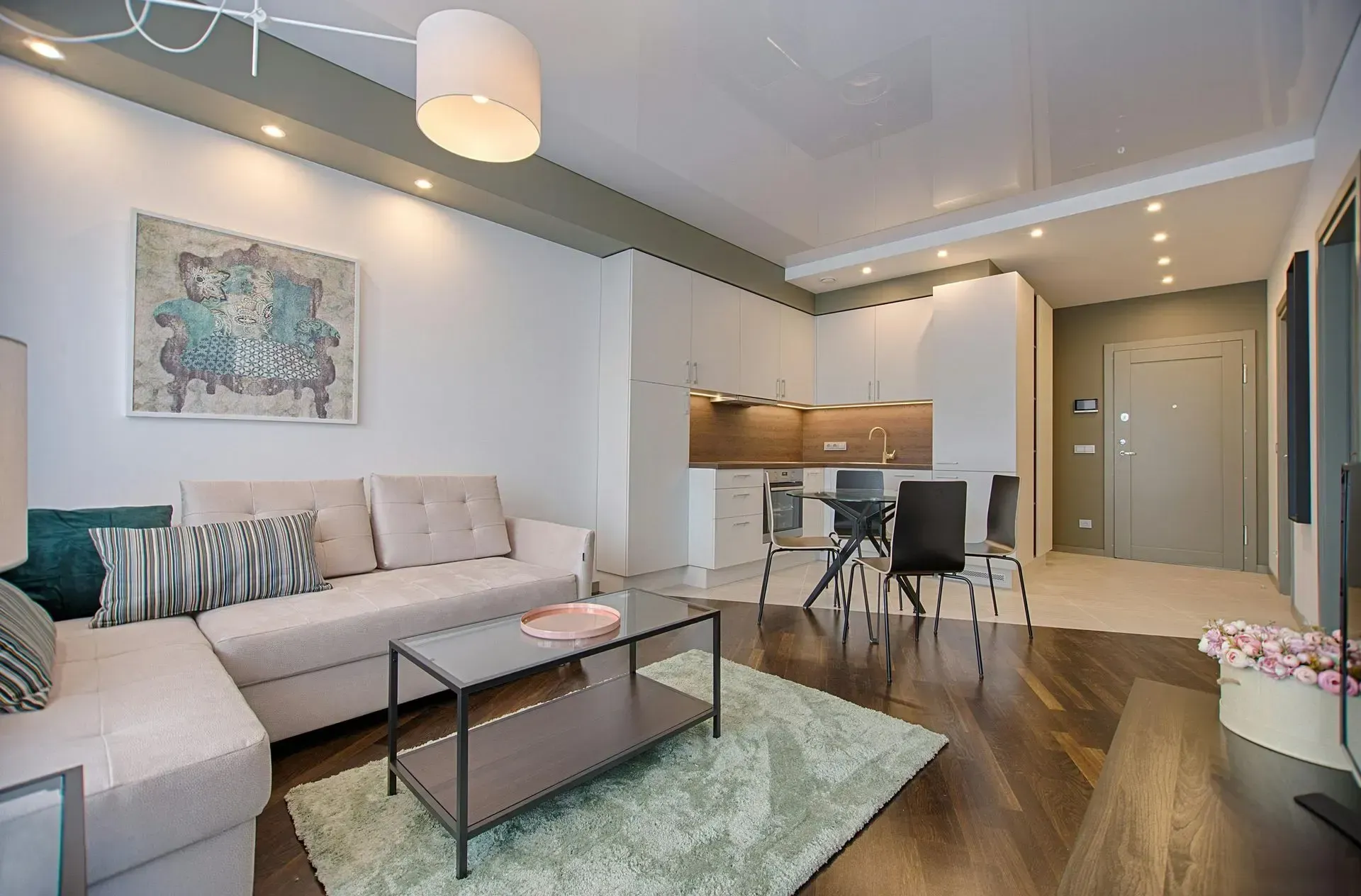 Apartamento moderno con sala de estar, sofá gris, cocina y TV.