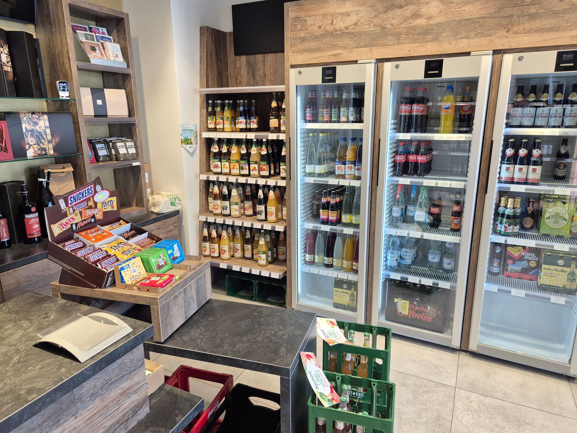Innenansicht eines Lebensmittelgeschäfts mit Snackauslagen und Getränkekühlschränken mit Glastüren.