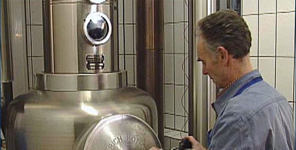 Ein Mann inspiziert einen großen industriellen Edelstahltank in einem Fabrikraum.