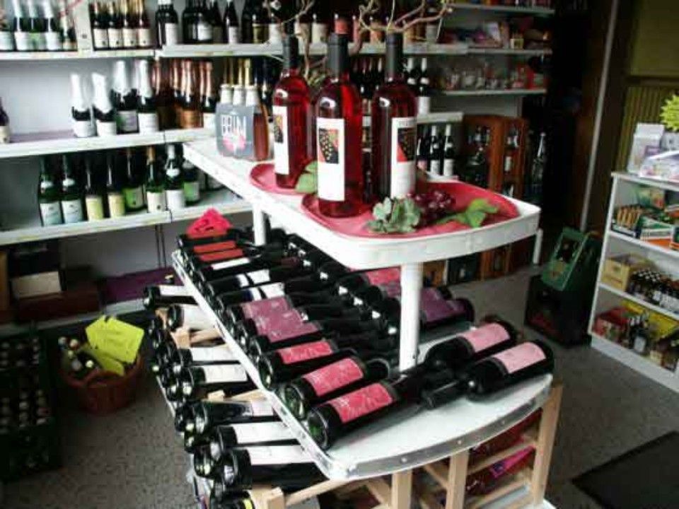 Weinflaschen sind in einem Ladenregal ausgestellt, davor steht ein weißer Tisch mit Rot- und Roséweinflaschen.