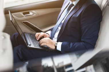 Un homme assis dans un taxi, qui tape sur le clavier de son ordinateur.