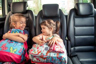 Des petites filles tenant leur cartable, assises dans un taxi.
