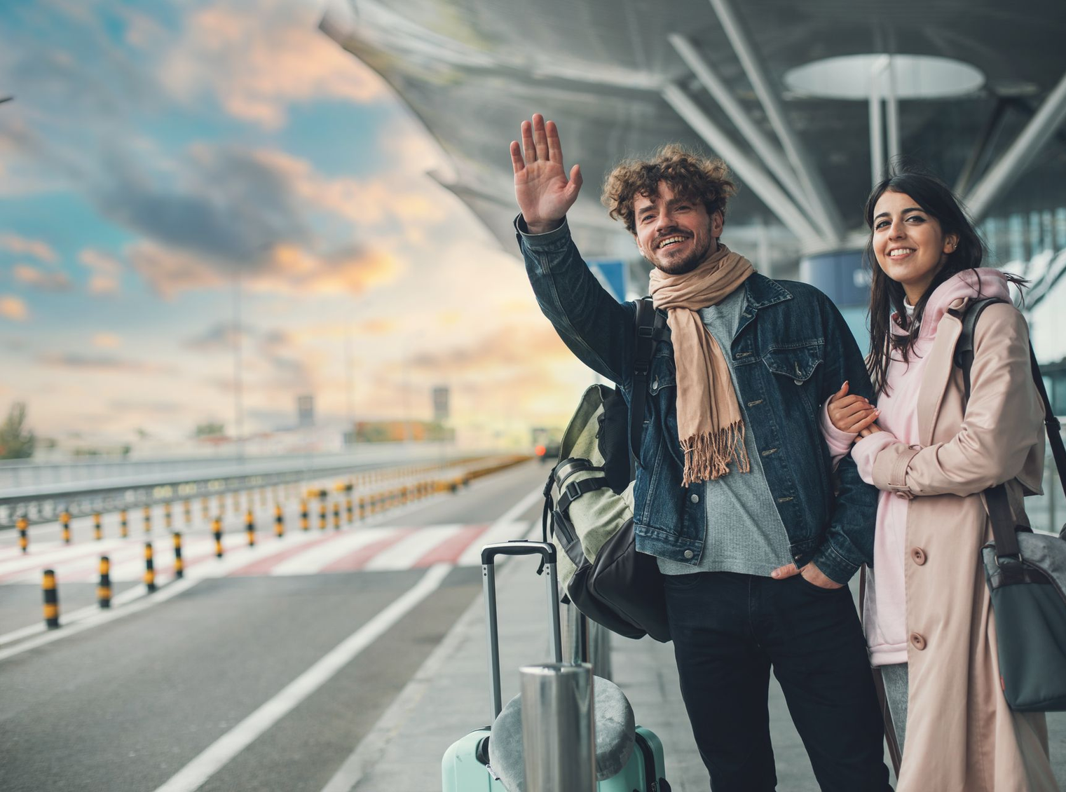 Un couple avec leurs bagages à l'entrée d'une gare, faisant signe à un taxi.