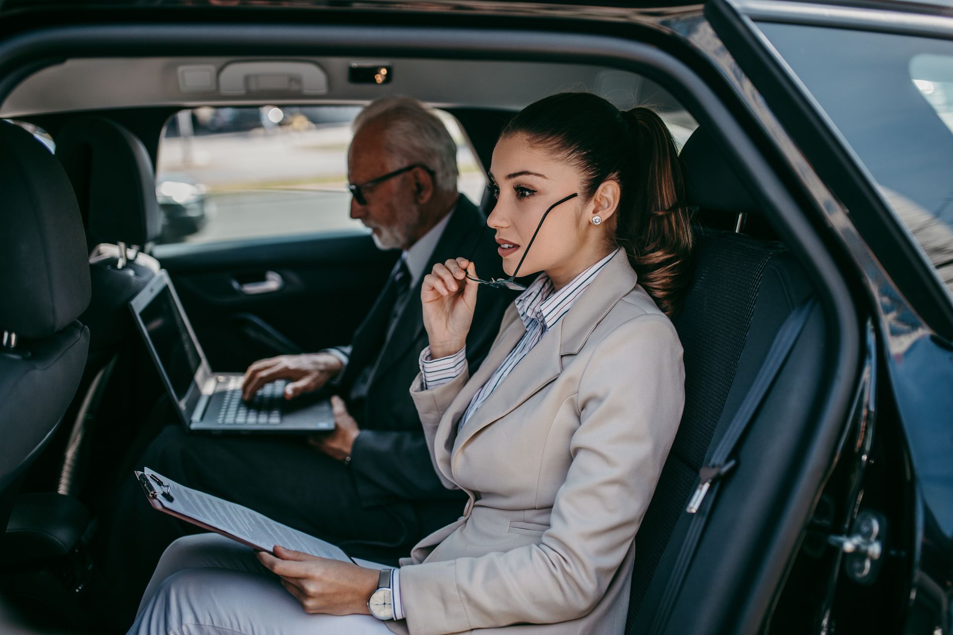 Deux professionnels dans un taxi, consultant des documents et un ordinateur portable pendant un trajet.