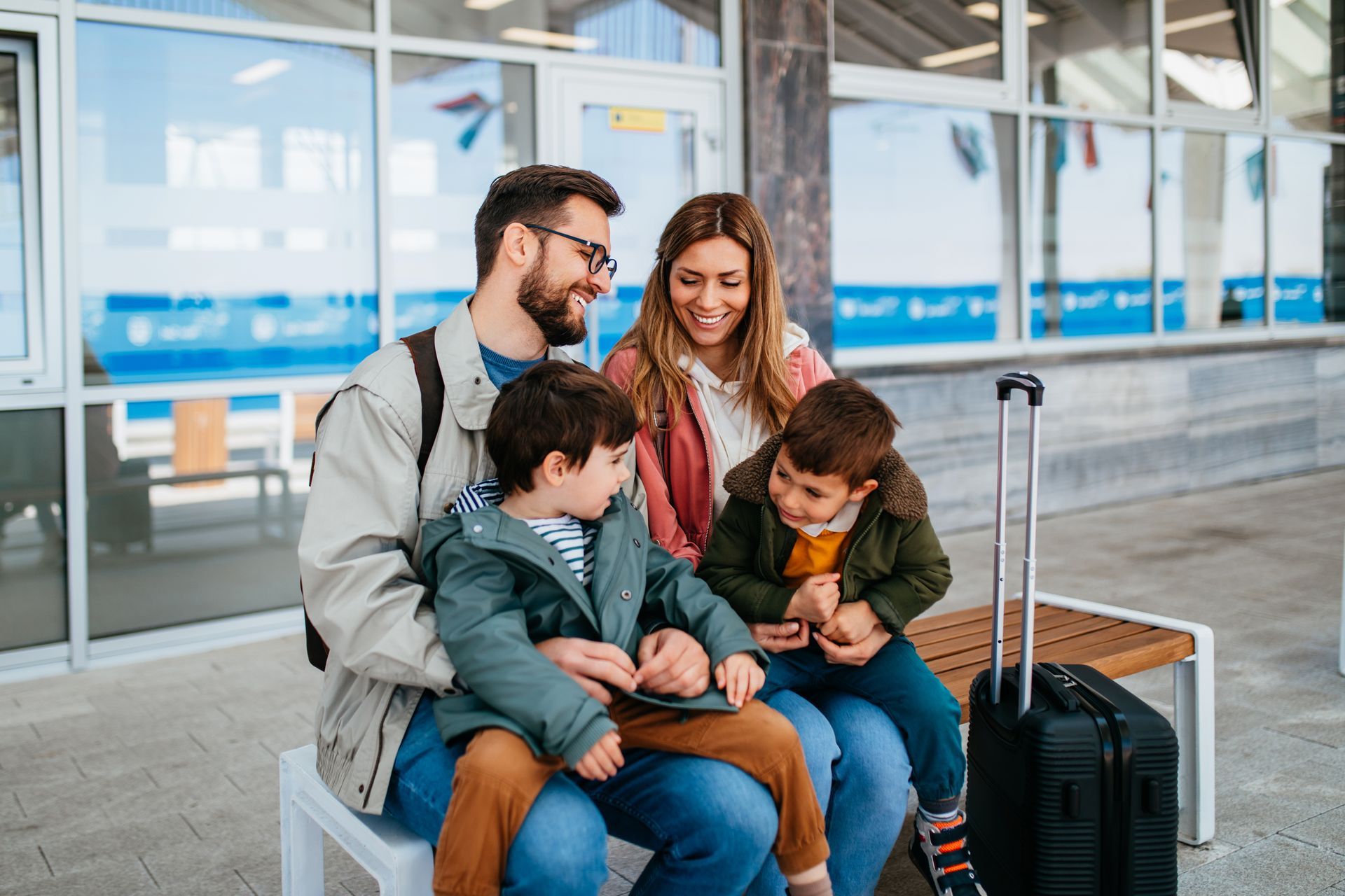 Une famille assise sur un banc, avec leurs bagages, à l'extérieur d'une gare.