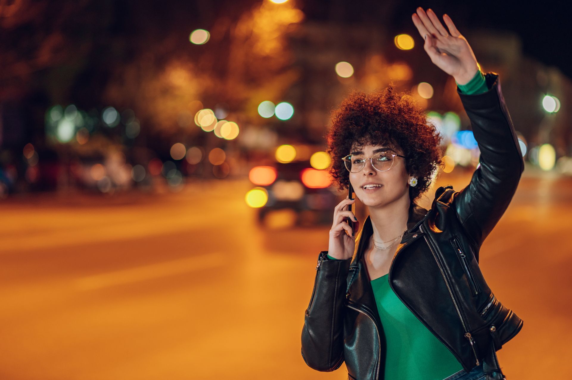 Dans la nuit, une femme au téléphone qui fait signe de la main à un taxi.