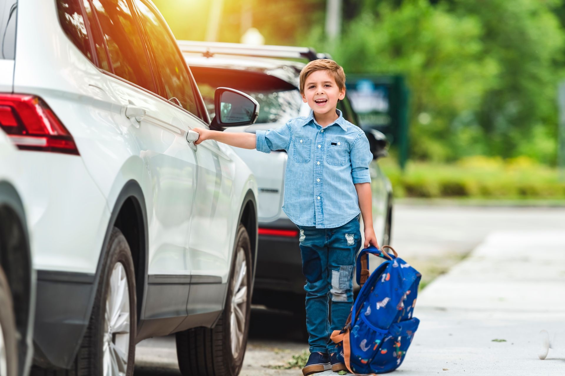 Un petit garçon qui tient son sac à dos dans une main et la poignée d'une voiture de l'autre.