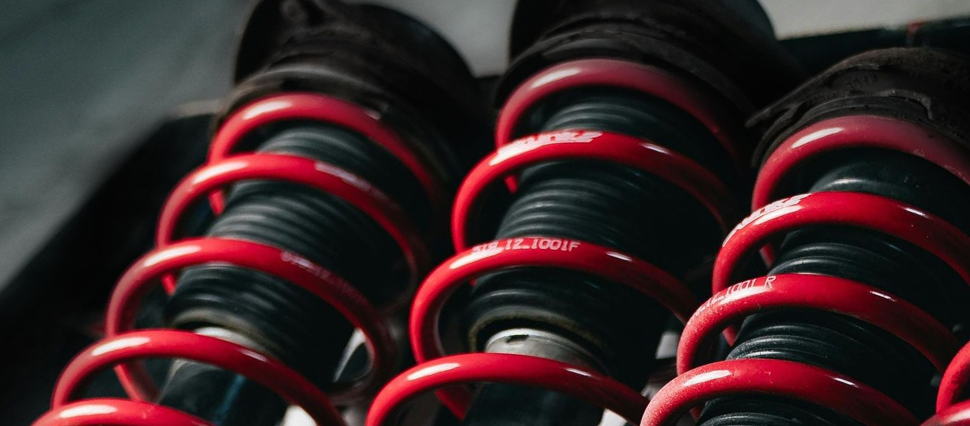 Quatro amortecedores com molas vermelhas, componentes enferrujados, sobre uma superfície preta.