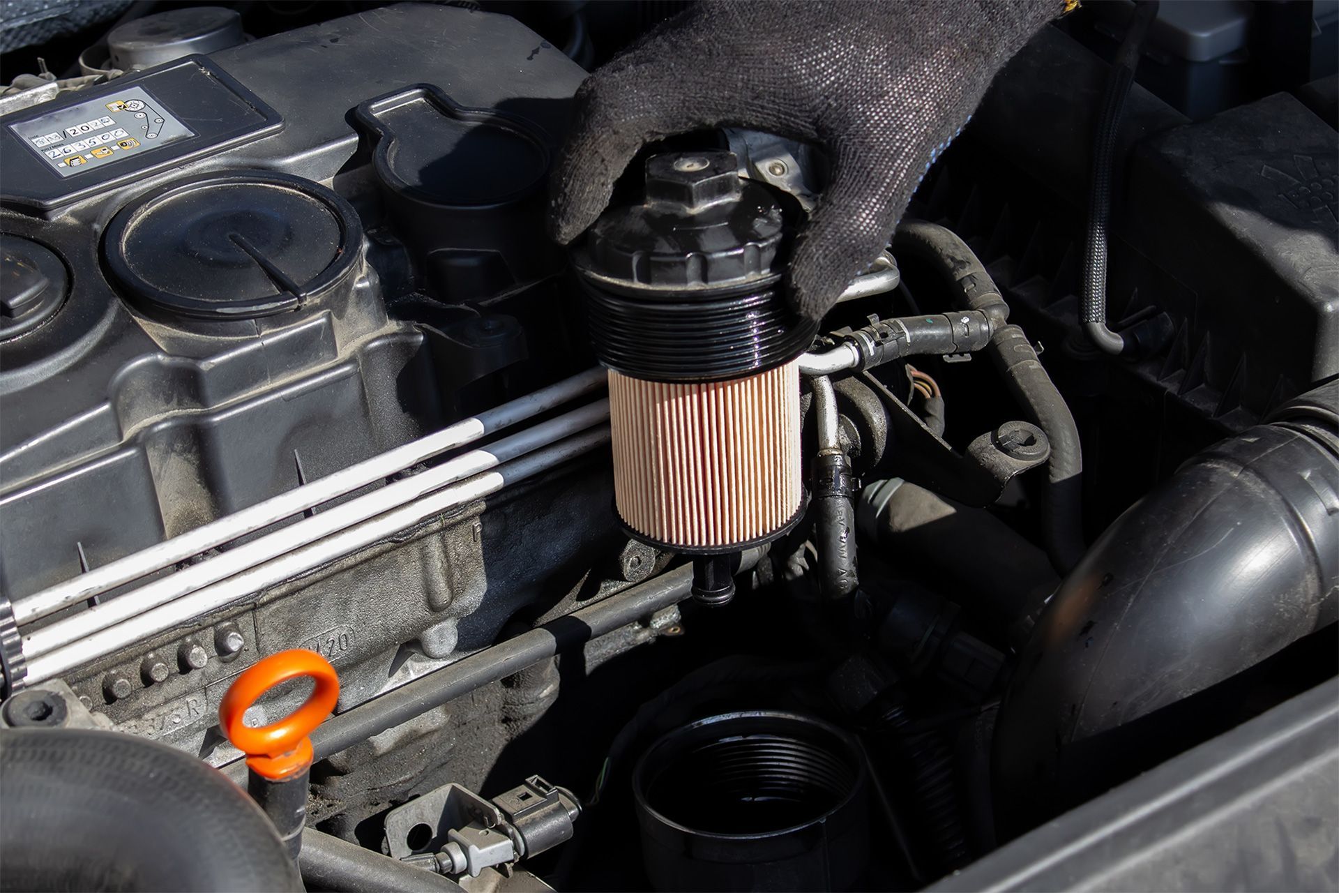 Três filtros de óleo cilíndricos com papel plissado amarelo e outras peças automotivas sobre uma superfície cinza.