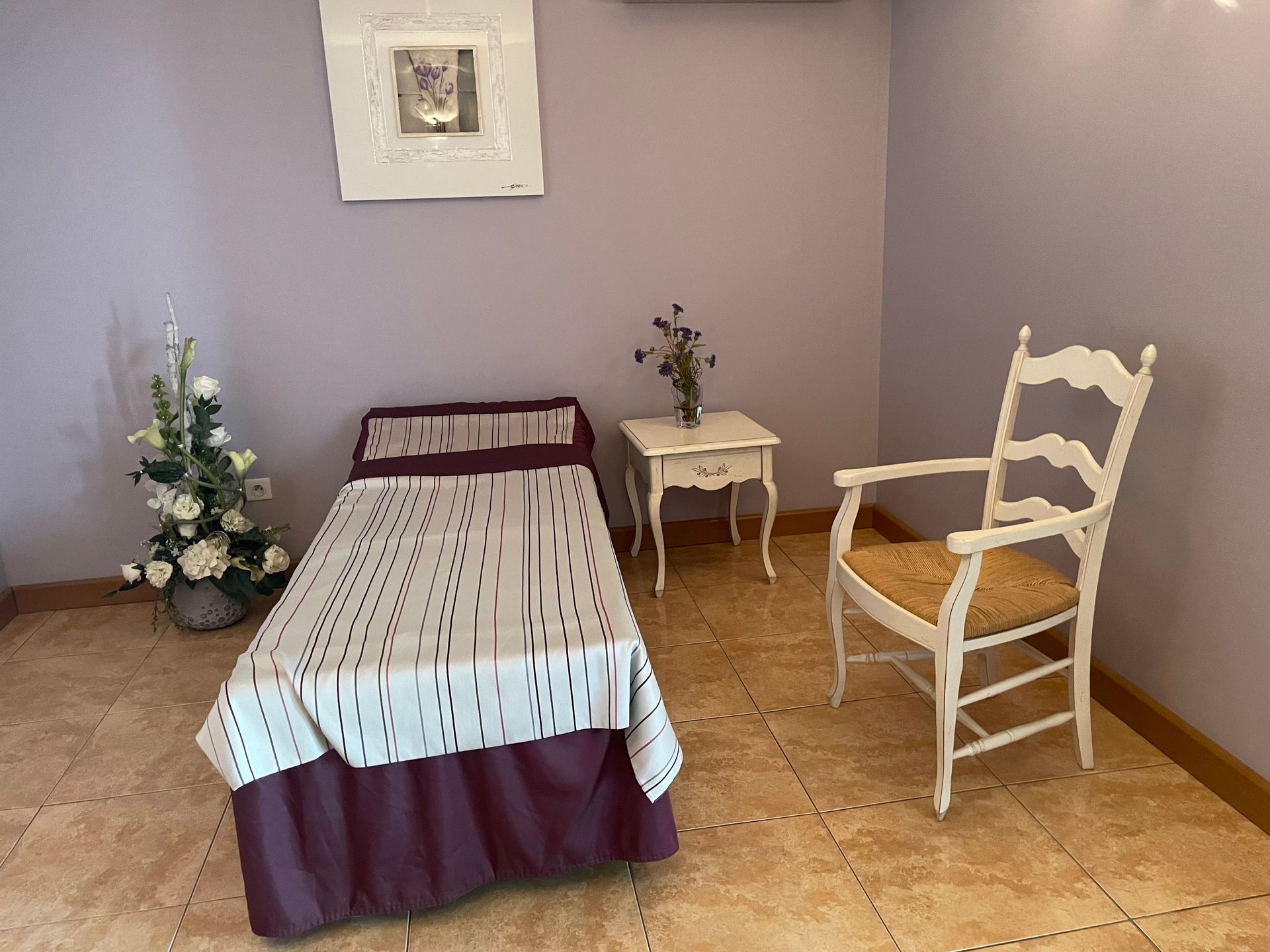 Chambre avec lit simple, chaise blanche, petite table avec des fleurs et art sur les murs violets.