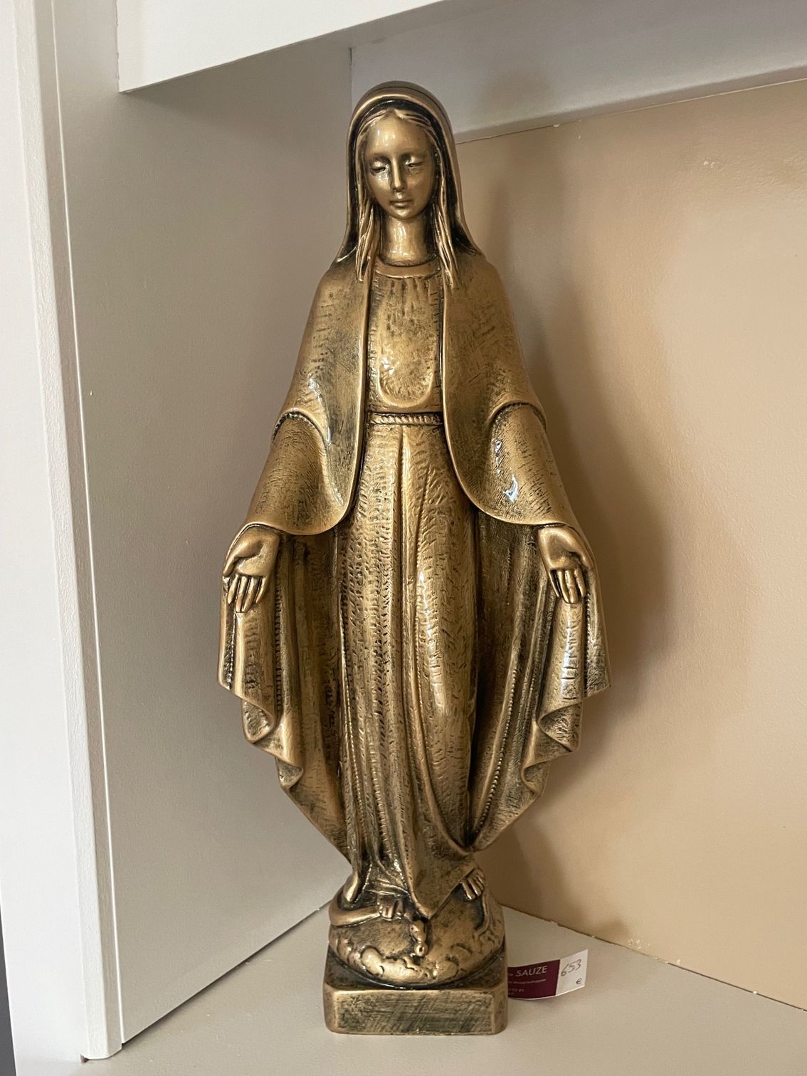 Statue en or de la Vierge Marie aux bras tendus, debout sur un socle.