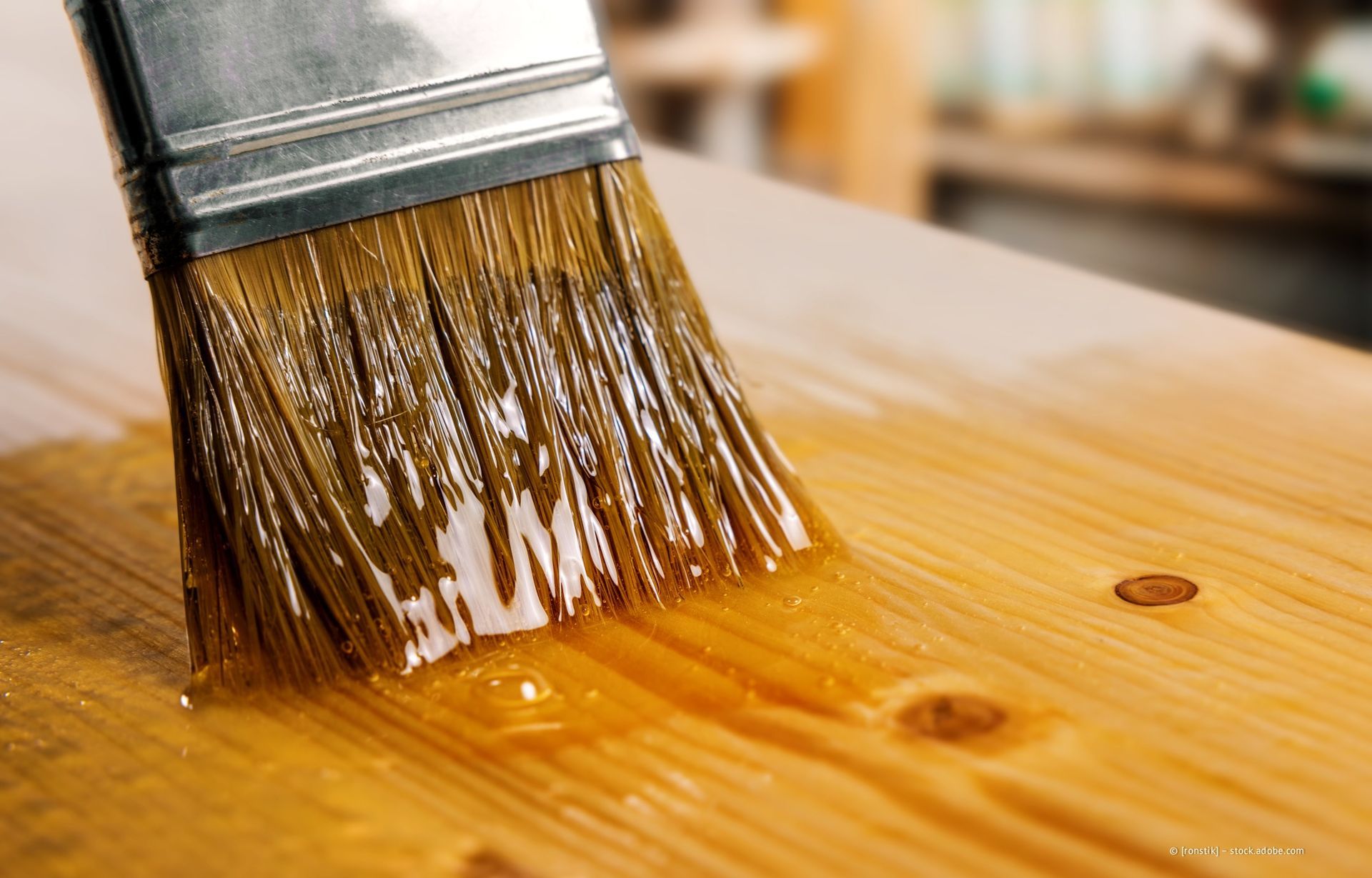 Mit einem Pinsel wird Lack auf die Holzoberfläche aufgetragen.