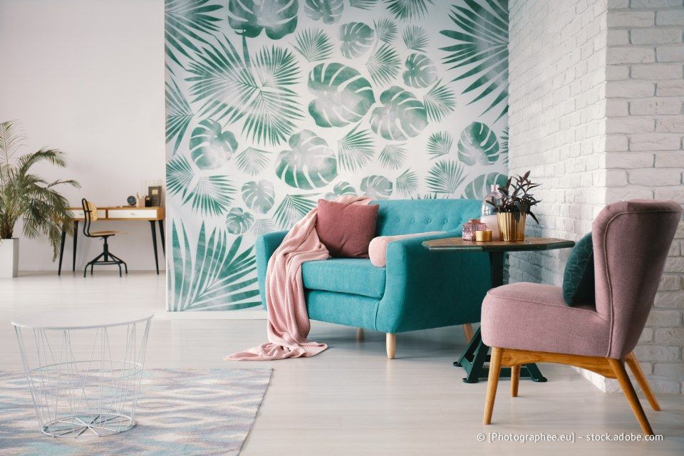 Wohnzimmer mit blaugrünem Sofa, rosa Sessel und Wand mit grünem Blattmuster.