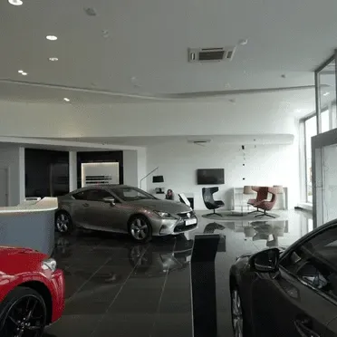 Una sala de exposición con un coche rojo y un coche gris.