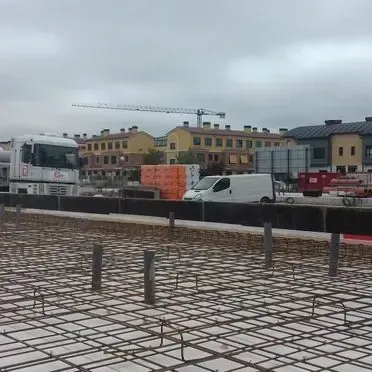 Una obra en construcción con un camión, una furgoneta y una grúa al fondo.