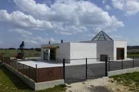Una casa blanca con techo en forma de pirámide está rodeada por una valla.