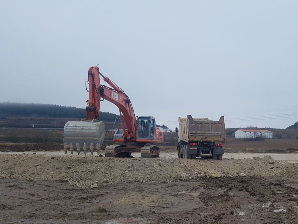 Una excavadora está cavando en un campo de tierra al lado de un camión volquete.