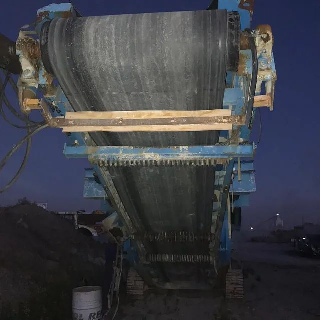 Una cinta transportadora está unida a una máquina en un campo por la noche.