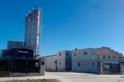 Un gran edificio con un silo al fondo y un cielo azul al fondo.