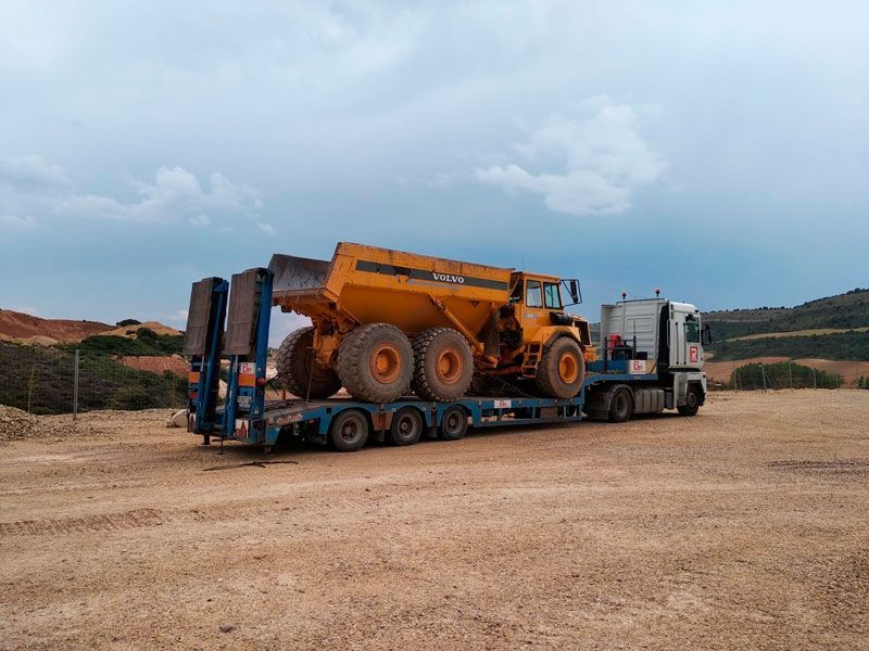 Un camión transporta un camión volquete sobre un remolque en un campo de tierra.