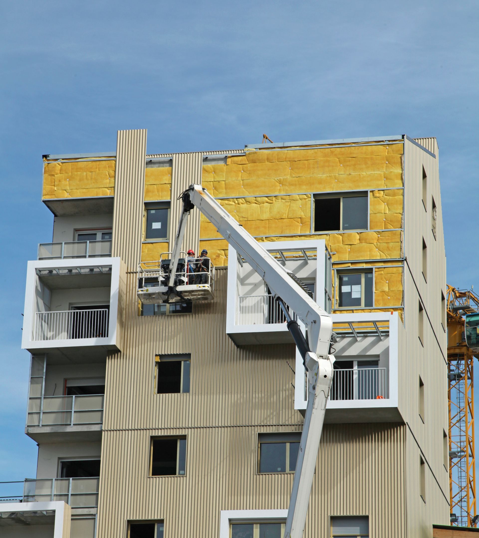 Construction d'une façade d'immeuble avec plateforme élévatrice ; isolation et pose de panneaux en cours.