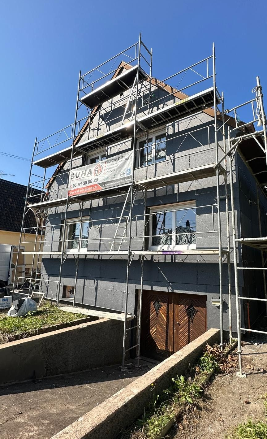 Maison à colombages de deux étages avec murs en stuc blanc, poutres brunes et volets foncés.