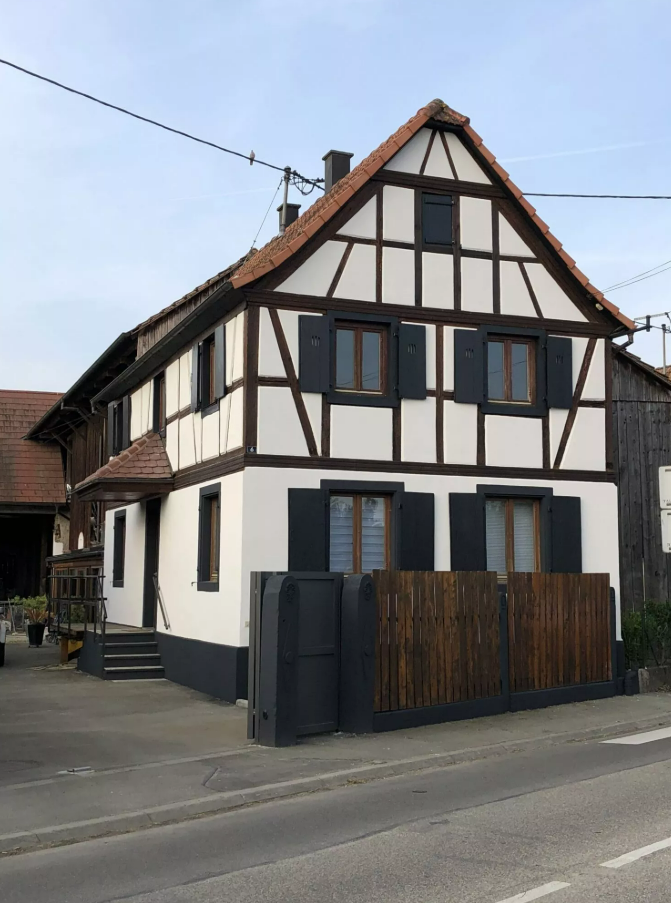 Maison blanche avec toit sombre et balcon, vue sur rue.
