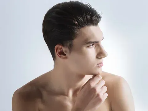 Un joven sin camisa con la mano en la barbilla mira hacia un lado.