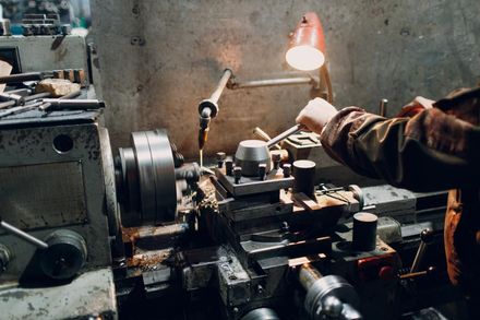Persona operando un torno en un taller, utilizando una llave inglesa e iluminado por una lámpara ajustable.