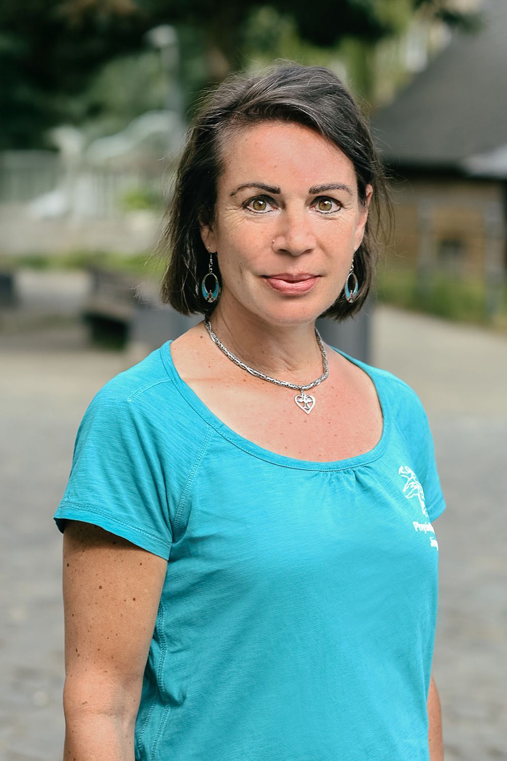 Porträt einer Frau in einem türkisfarbenen Hemd, die im Freien steht, vor verschwommenem Hintergrund.
