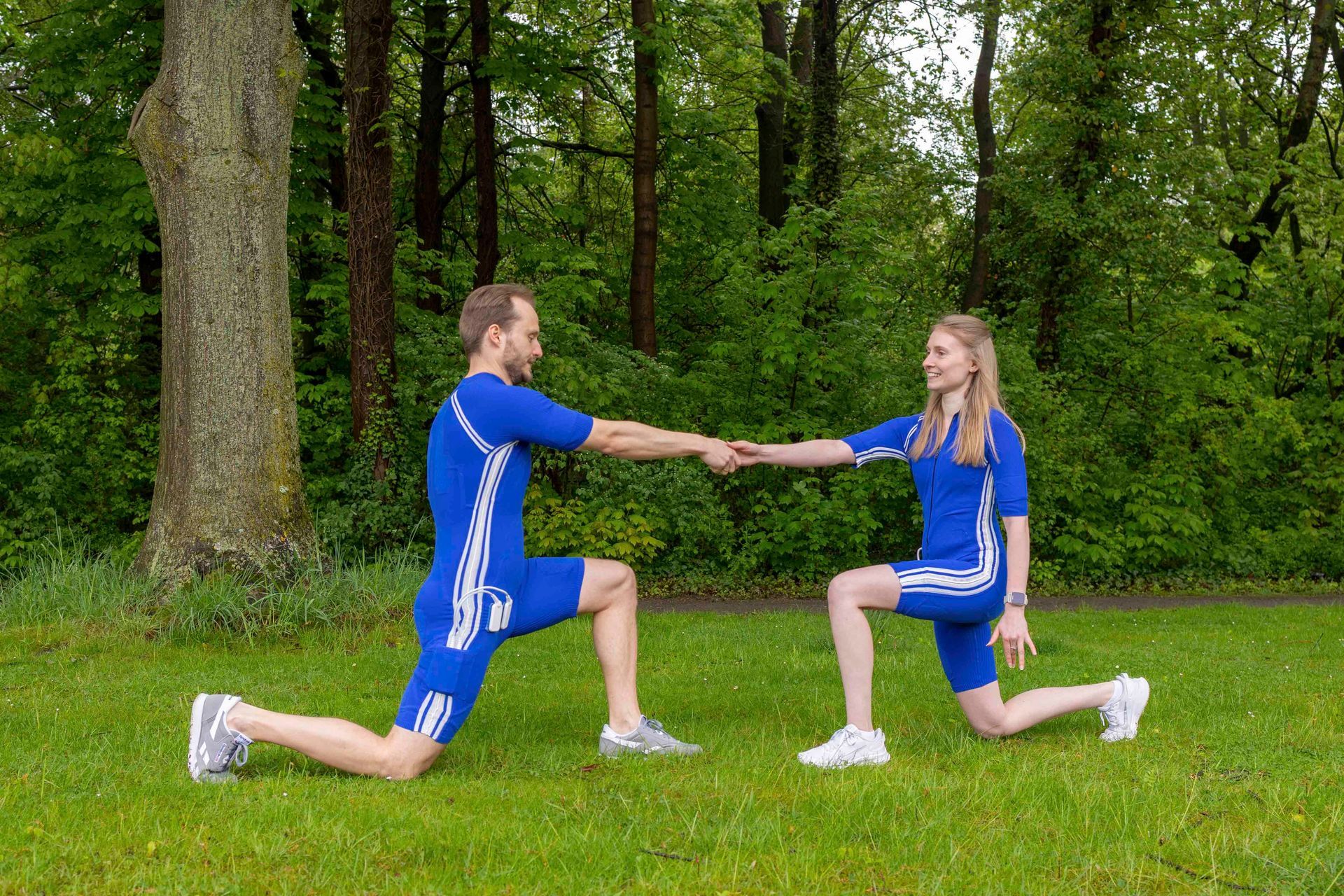 Zwei Athleten in blauen Uniformen stürzen sich in einem grasbewachsenen Park aufeinander zu und halten dabei ihre Fäuste