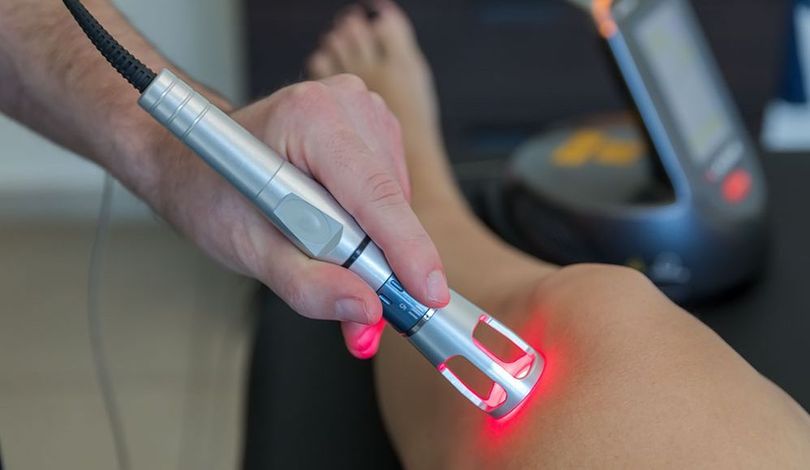 Nahaufnahme eines Therapeuten, der während der Behandlung ein Handgerät am Knie eines Patienten verwendet.