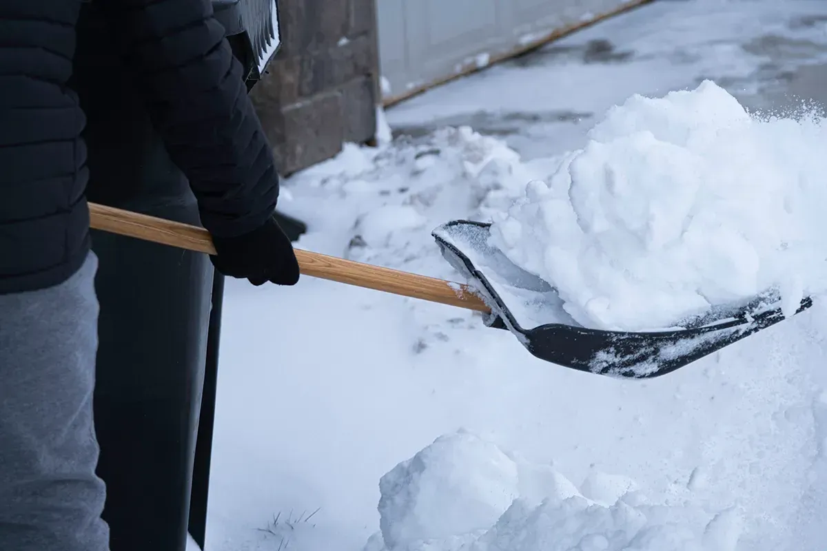 Eine Person schaufelt mit einer Schaufel Schnee vom Boden.