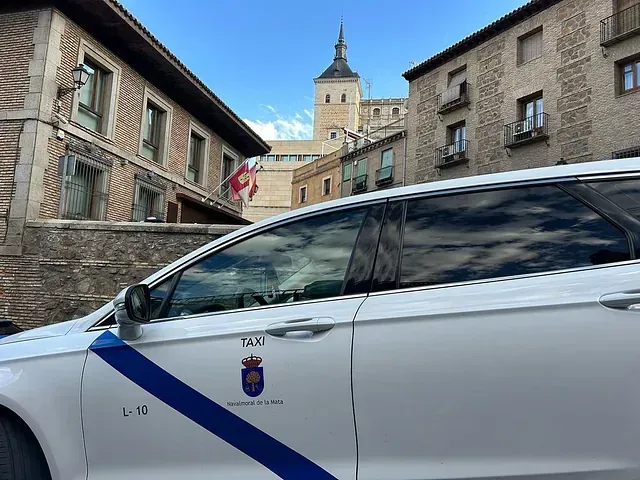 Un coche blanco con una franja azul en el lateral está aparcado delante de un edificio.