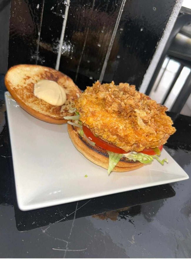 Sándwich de pollo frito crujiente en un plato blanco con lechuga, tomate y pan tostado.