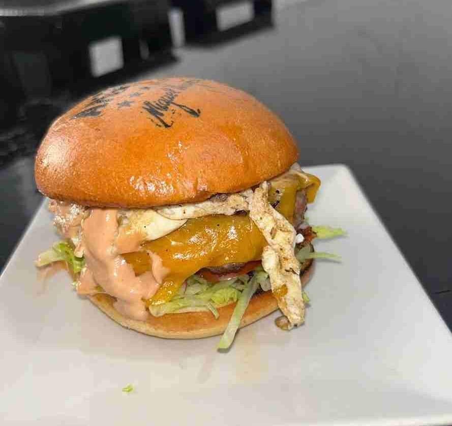Hamburguesa con pan dorado, queso, salsa y huevo frito en un plato blanco.