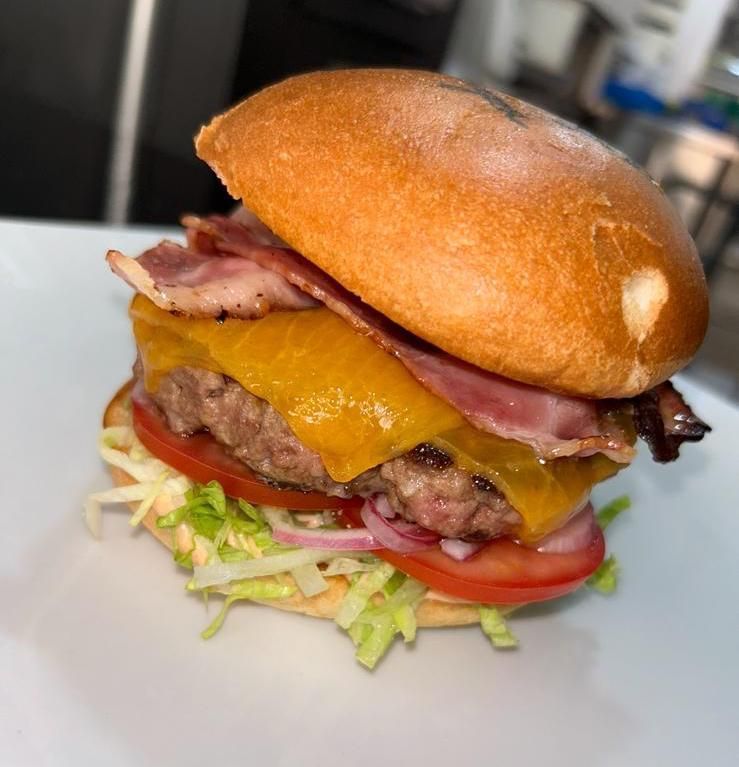 Hamburguesa con queso en un plato blanco con tocino, lechuga, tomate y cebolla roja.