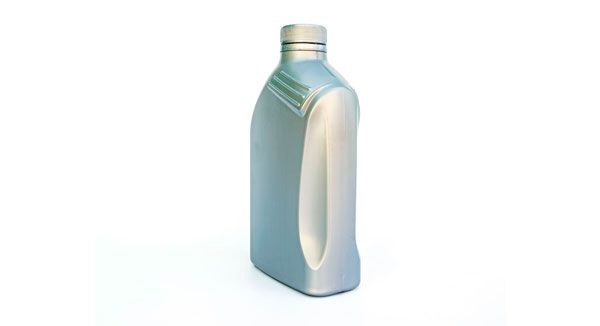Una botella de aceite reposa sobre una superficie blanca.