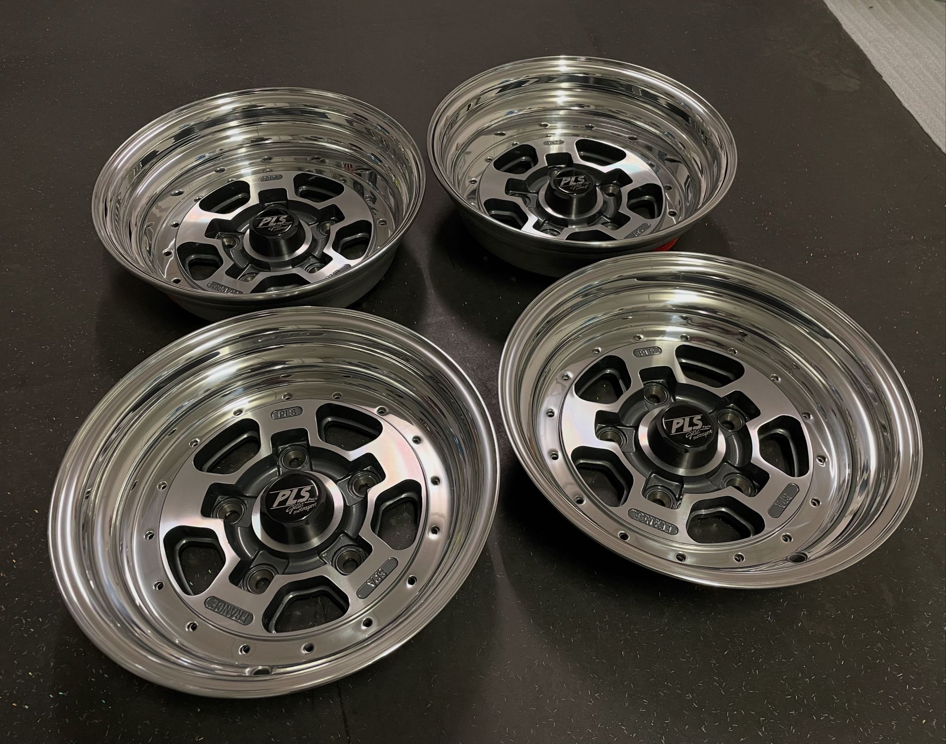 Vier glänzende silber-schwarze LKW-Felgen auf dunklem Untergrund.
